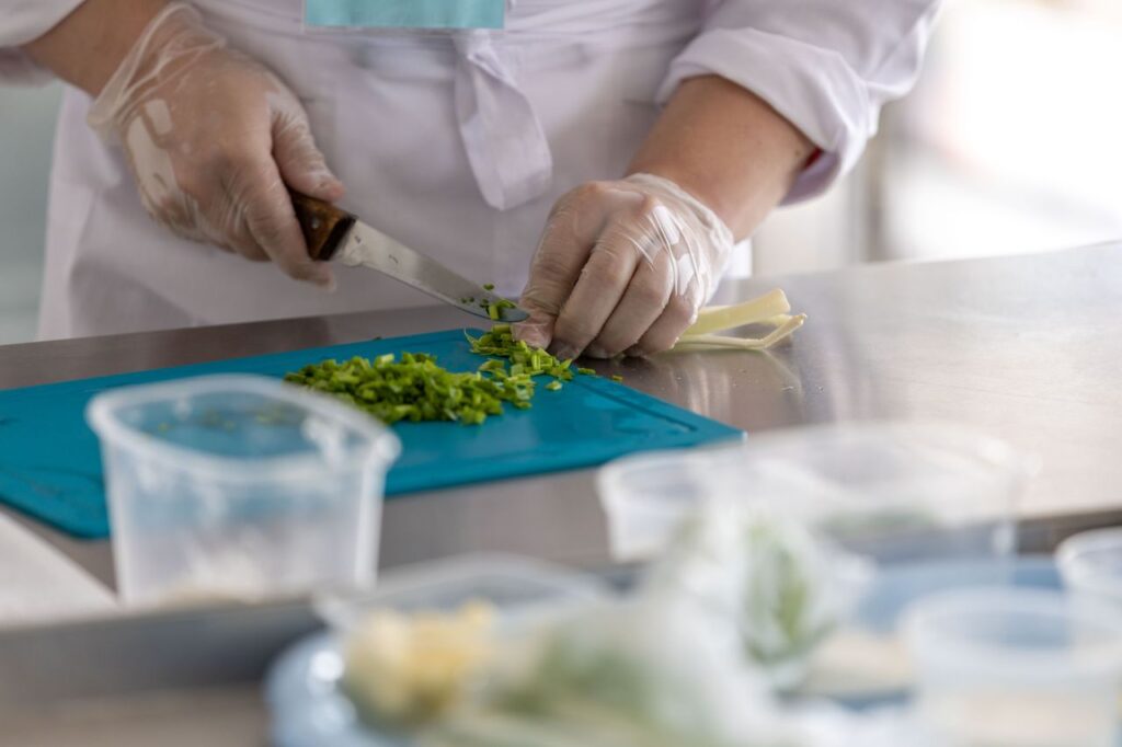 A chef expertly chops fresh herbs on a blue cutting board in a professional kitchen environment.
