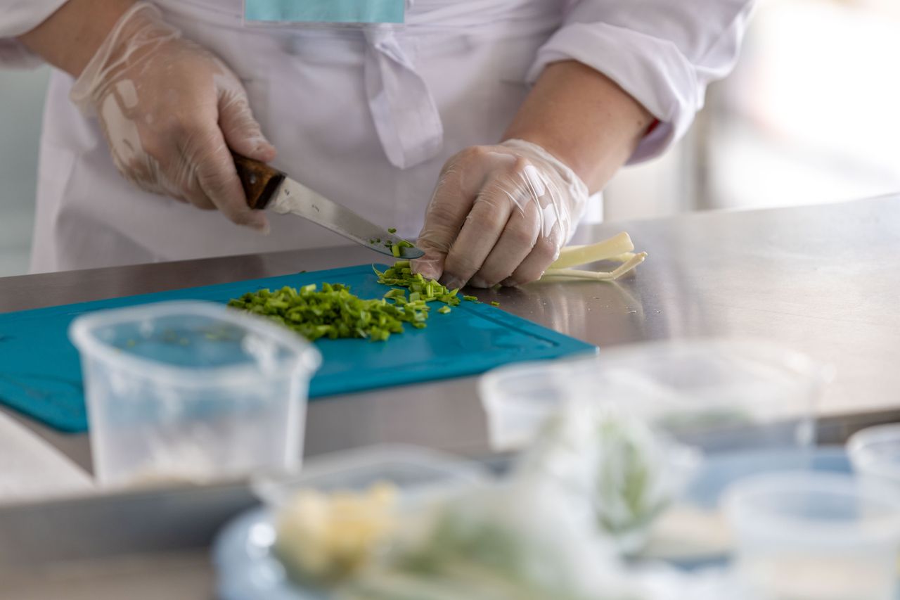 A chef expertly chops fresh herbs on a blue cutting board in a professional kitchen environment.