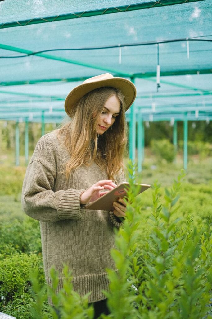 Woman surfing tablet and checking information while working in greenhouse with different green plants