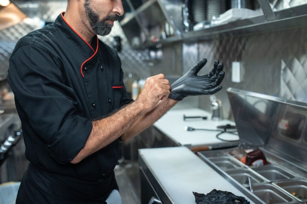 Chef putting on gloves in a professional kitchen setting, emphasizing hygiene and readiness.